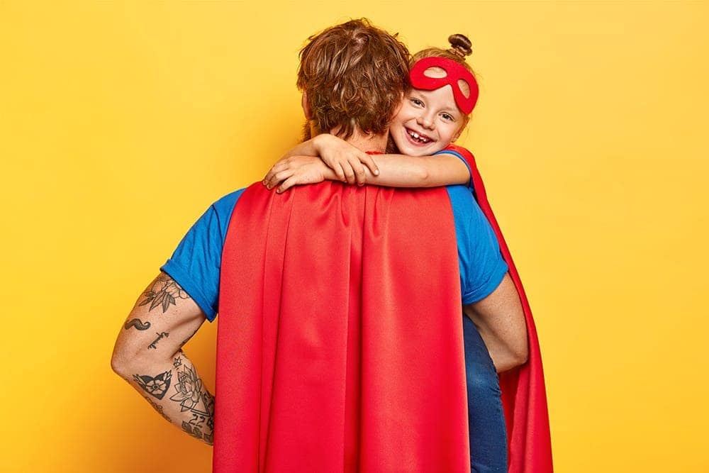 Dad dressed with superman cape cuddling daughter